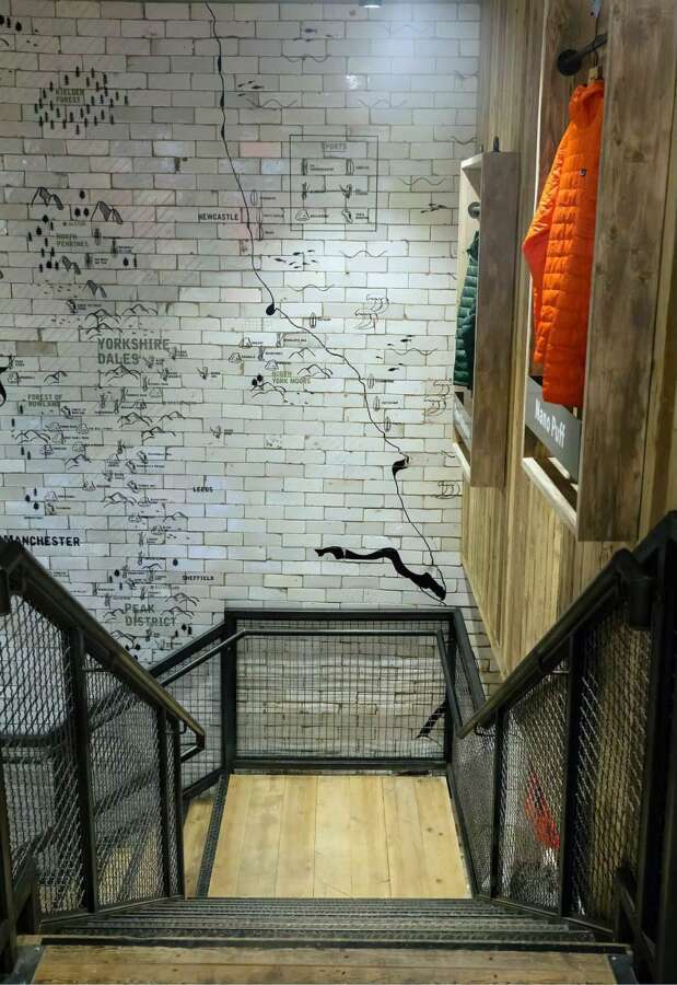 Vertical view of hand painted map artwork across tiled stairwell walls in Patagonia Manchester store