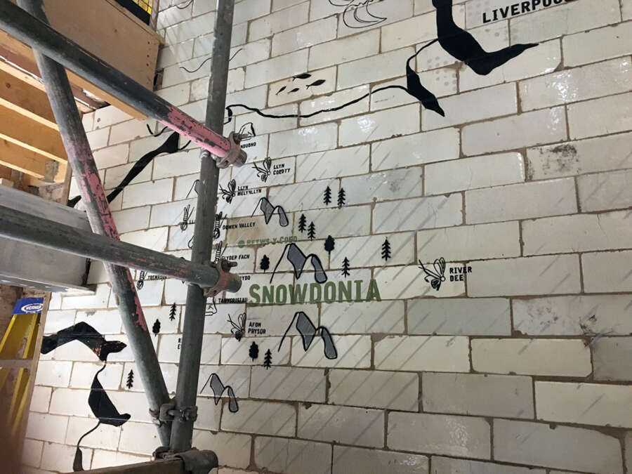 Installation of painted wall graphics across reclaimed tile surface in Patagonia Manchester store stairwell