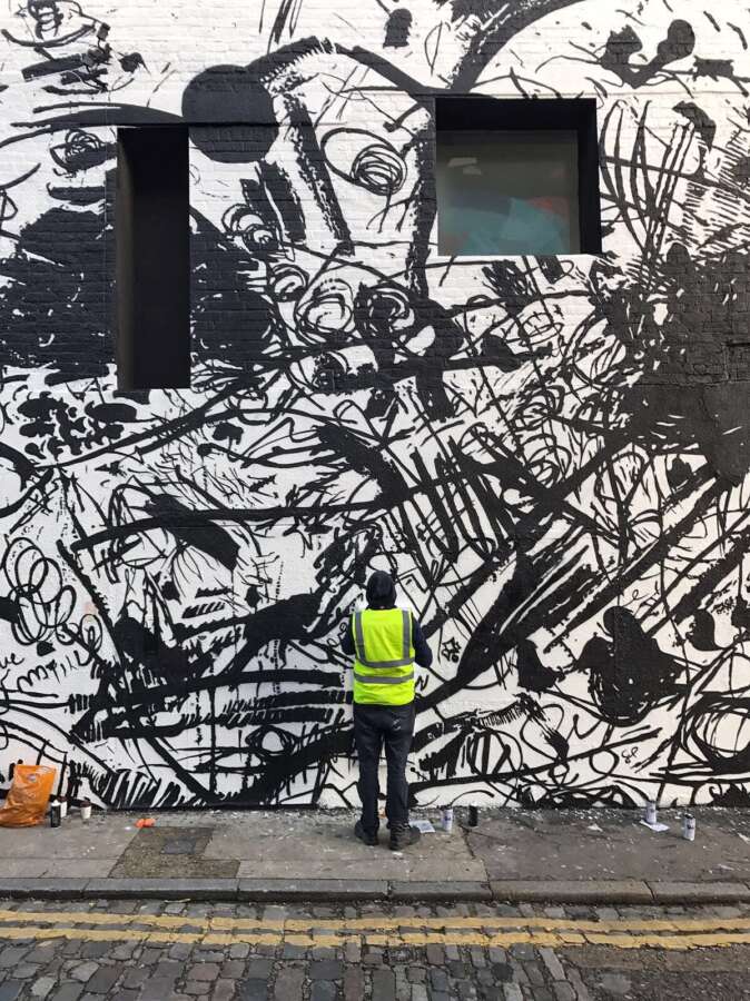 Artist painting the Feinschmecker mural by Sue Webster on the Dirty House building