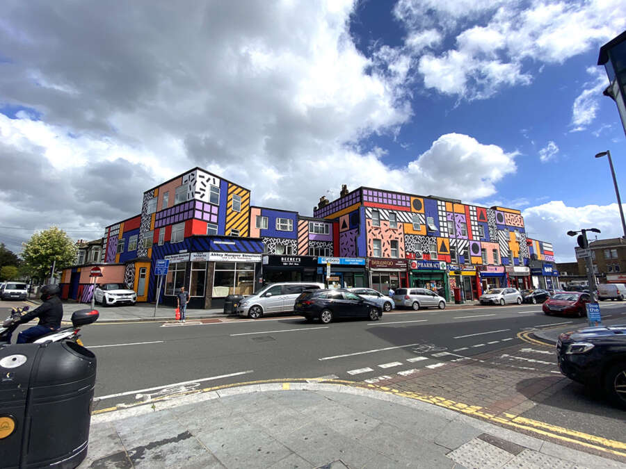 Corner view of Camille Walala’s Walala Parade mural wrapping multiple buildings on Leyton High Road