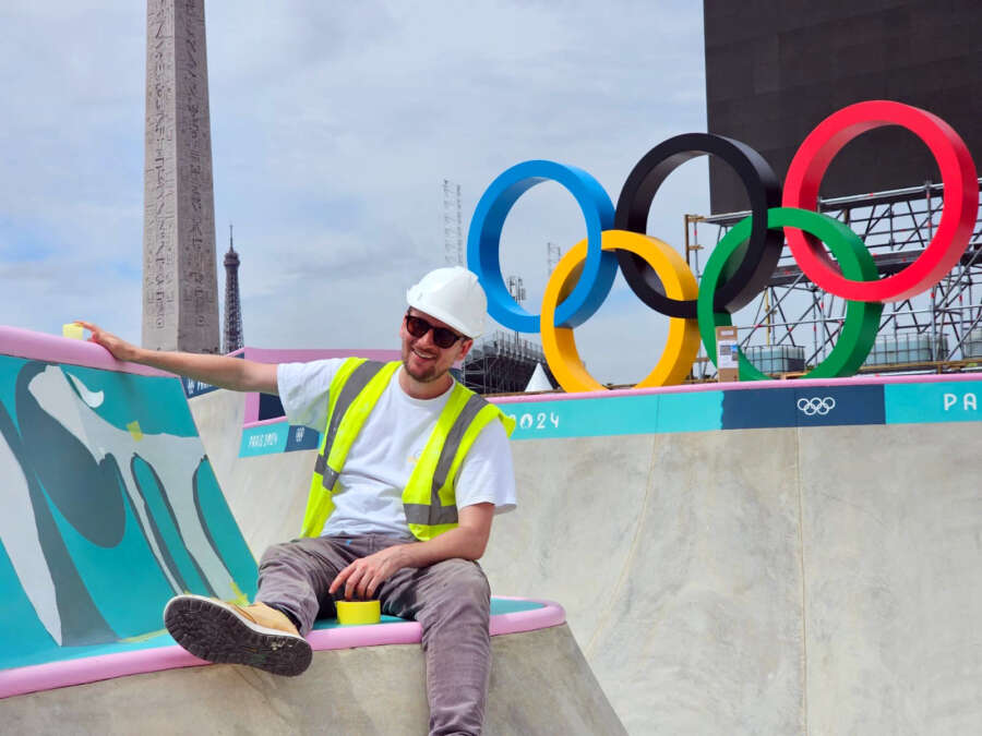 Crew member sitting inside Paris 2024 Olympic skatepark during mural installation