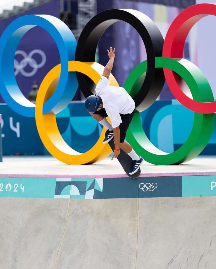 Skateboarder performing trick in front of Olympic rings at the Paris 2024 skatepark
