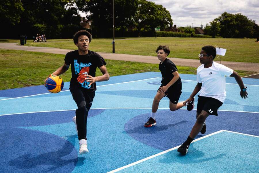 Young people playing basketball on Darren John painted court mural in Barnet park