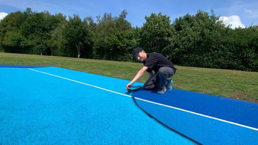 Darren John painting lines on outdoor basketball court mural in Barnet, North London