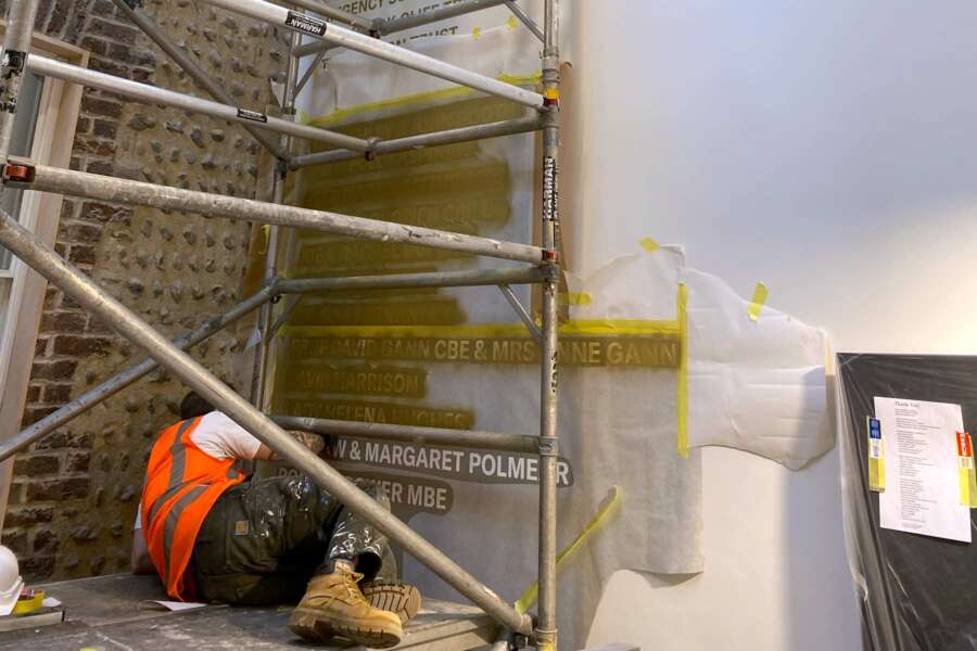 Work in progress hand painting donor wall lettering from scaffold inside Brighton Dome