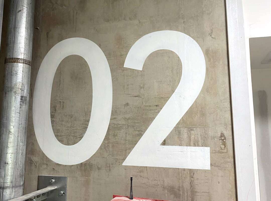 Hand painted floor level signage number 02 on concrete stairwell wall Large hand painted floor level indicator 02 applied directly to exposed concrete wall in fire escape stairwell