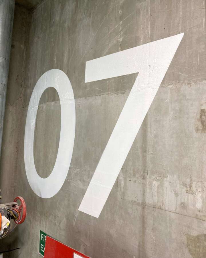 Hand painted floor level indicator 07 on raw concrete wall inside fire escape stairwell