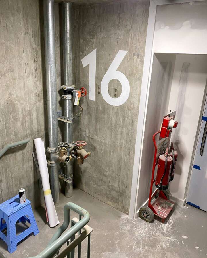 Large painted floor number 16 applied to exposed concrete wall in student accommodation stairwell