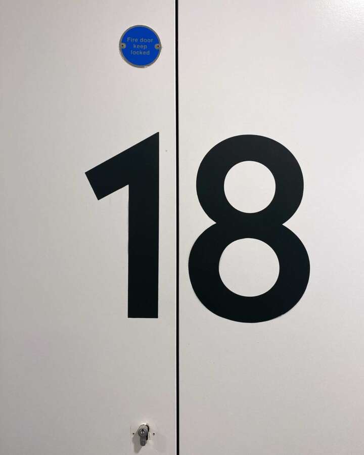 Close-up of hand painted cupboard door number 18 used as corridor wayfinding marker